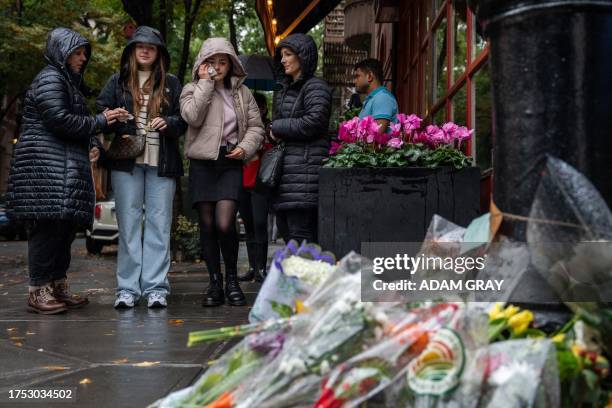 People stand before flower tributes to actor Matthew Perry outside the apartment building which was used as the exterior shot in the TV show...