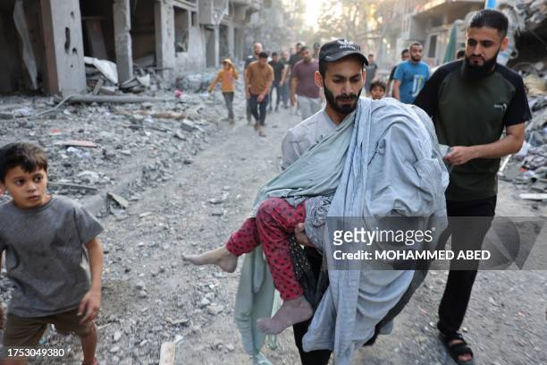 Graphic content / TOPSHOT - A Palestinian man carries the covered body of a girl removed from the rubble of a building following the Israeli...