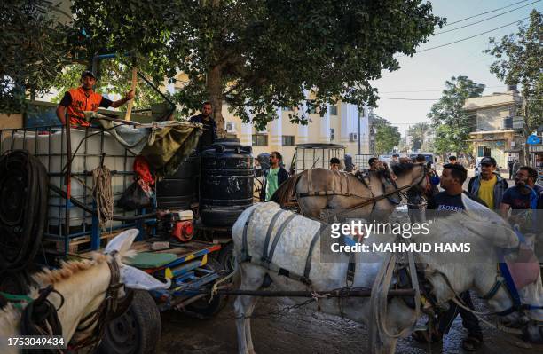 Palestinians gather next to donkey-drawn carts loaded with water tanks for sale, as drinking water and fuel become increasingly scarce, in Khan Yunis...