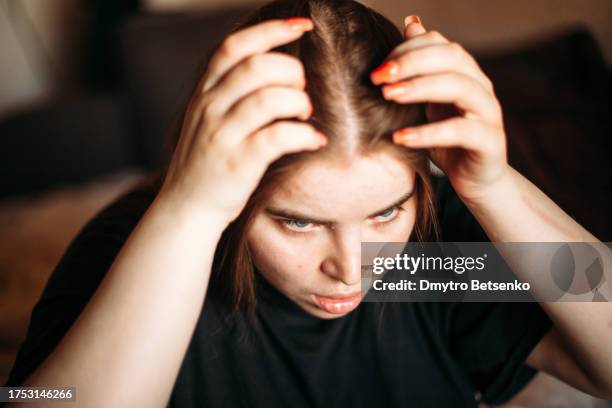 young woman parting hair looking in the mirror at home - hair parting stockfoto's en -beelden