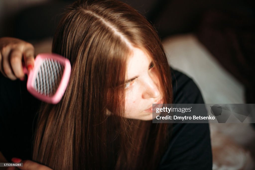 Beautiful young woman brushing her hair at home