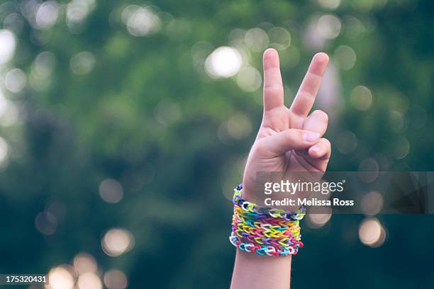 hand with friendship bracelets making peace sign - friendship bracelet stock pictures, royalty-free photos & images