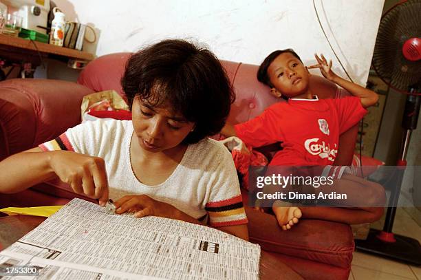 Endang Isnani learns how to sew while her oldest son, Garil Arnanda sits behind her in the living room of their home January 30, 2003 in Denpasar,...