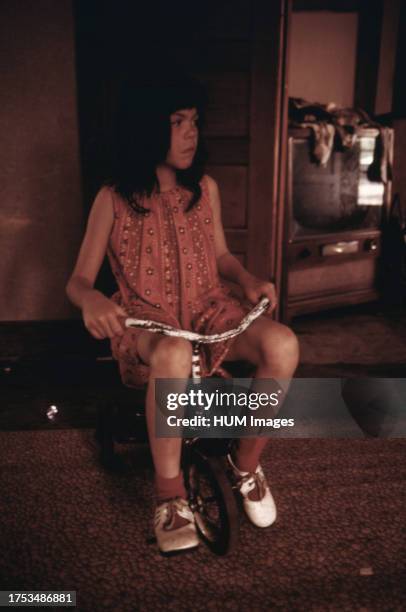 Diane Watkins finds the living room of their new home big enough to ride her tricycle in ca. 1975.