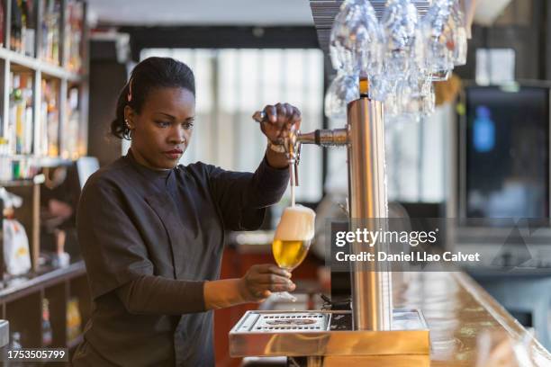 female bartender pouring beer into a glass from the tap at the bar counter. - waiter stock pictures, royalty-free photos & images