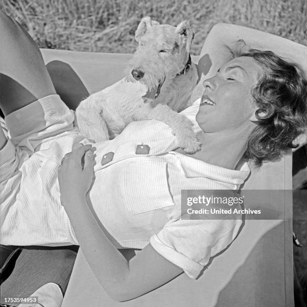 Young woman lying by the folding roof of a Ford V8 convertible with her fox terrier pup, Germany 1930s.