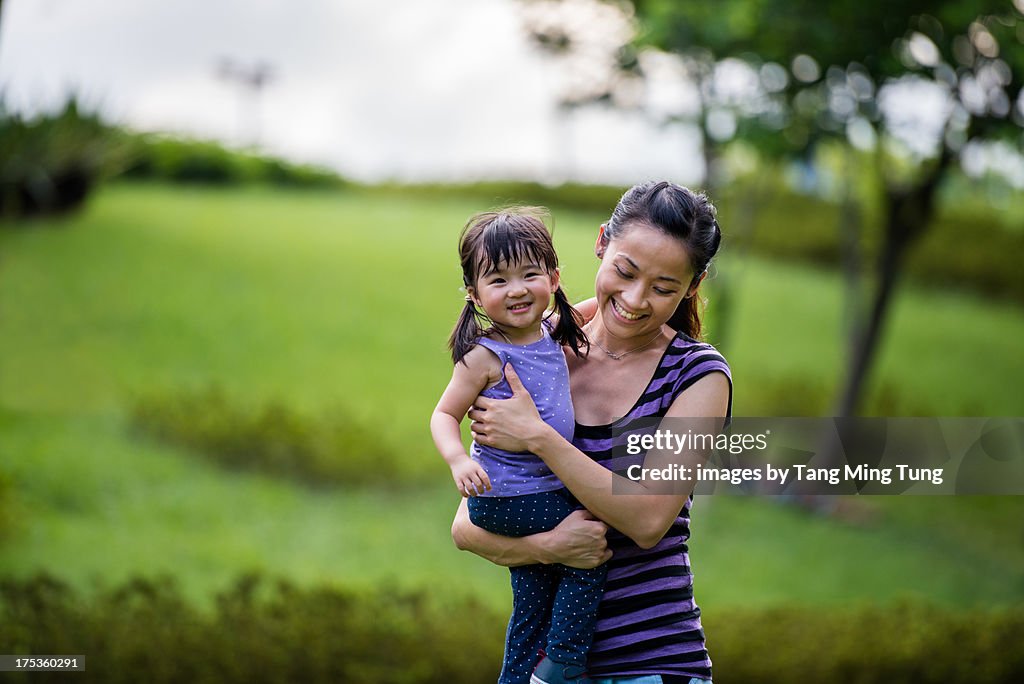 Young mom holding toddler strolling in the park