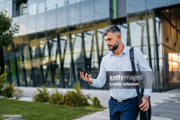 adult man leaving his office and checking his phone - closing time stock pictures, royalty-free photos & images