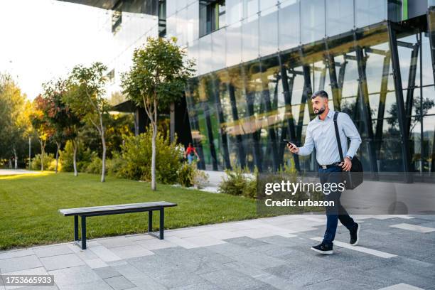 hombre adulto saliendo de su oficina y revisando su teléfono - maletín para portátil fotografías e imágenes de stock