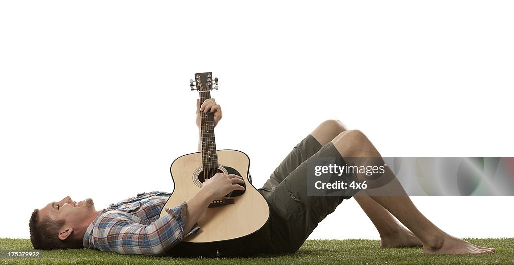 Man lying on the grass and playing a guitar