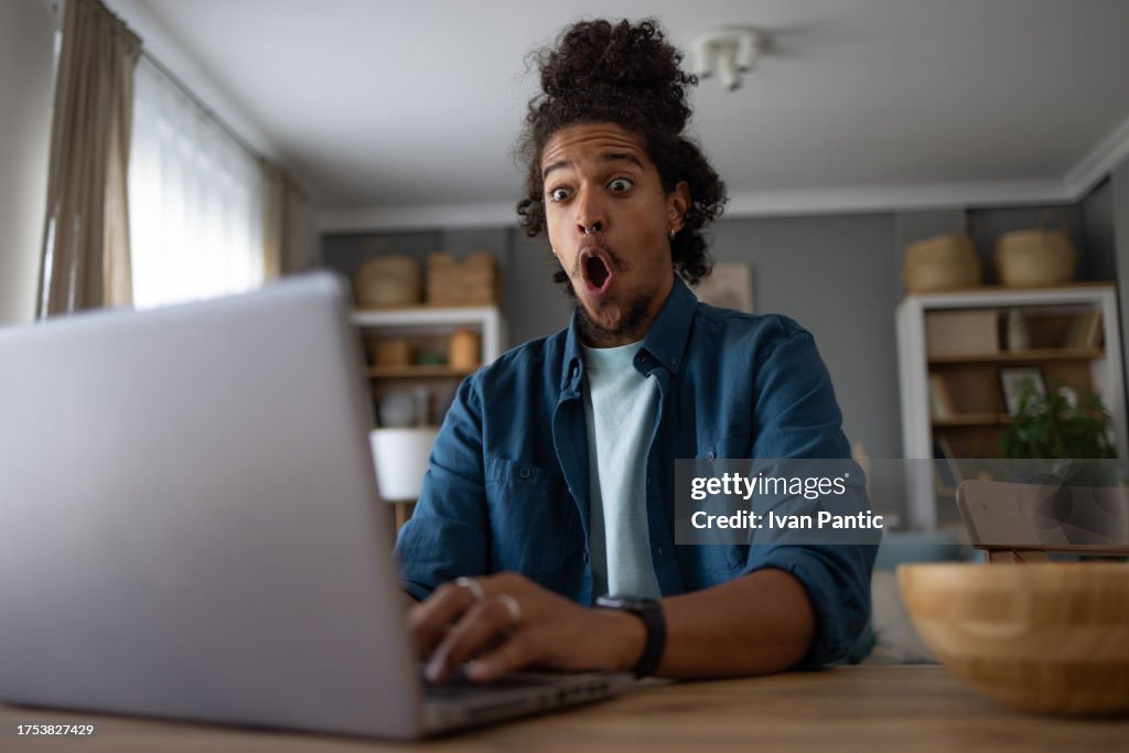 Shocked black man working on laptop at home office.