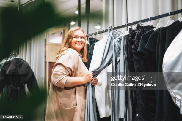 young beautiful woman plus size chooses clothes at store - kledingwinkel stockfoto's en -beelden