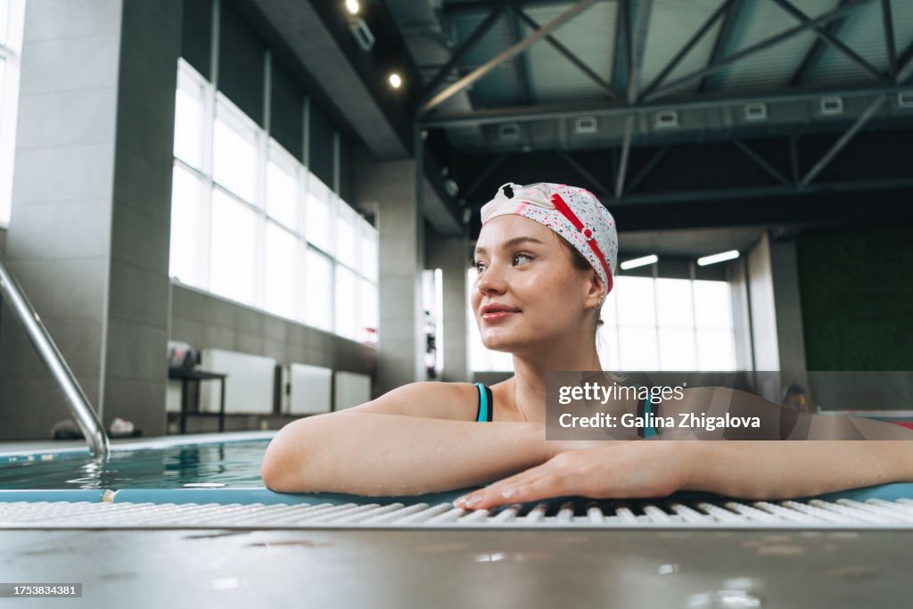 Young smiling woman in blue swimsuit swimming in sports pool