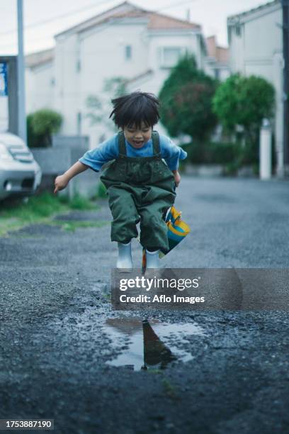japanese kid playing outside on a rainy day - charco fotografías e imágenes de stock