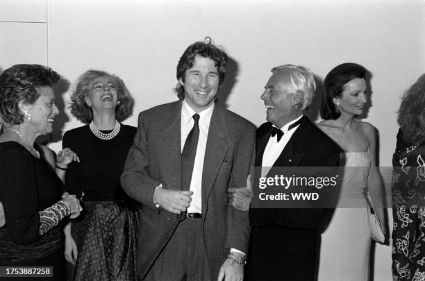 Actor Richard Gere shows designer Giorgio Armani his suit label, as guests watch the exchange, with socialite Lee Radziwill.