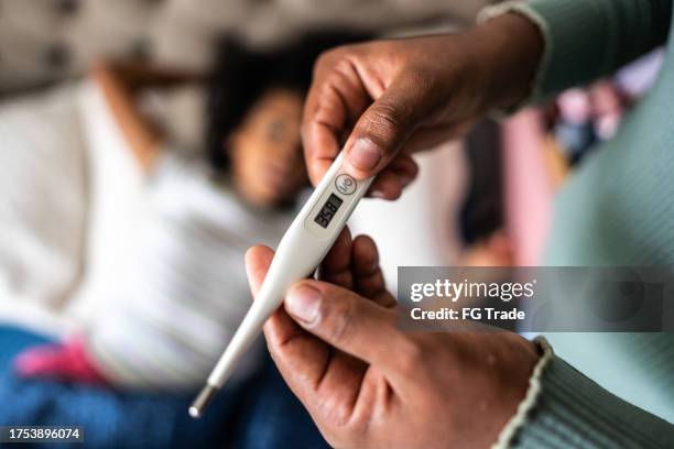 primer plano de las manos de la madre comprobando la temperatura con el termómetro en casa - termometro fotografías e imágenes de stock