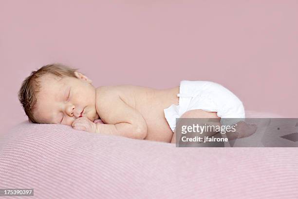 full length newborn baby girl asleep on tummy. pink background. - diapers stockfoto's en -beelden