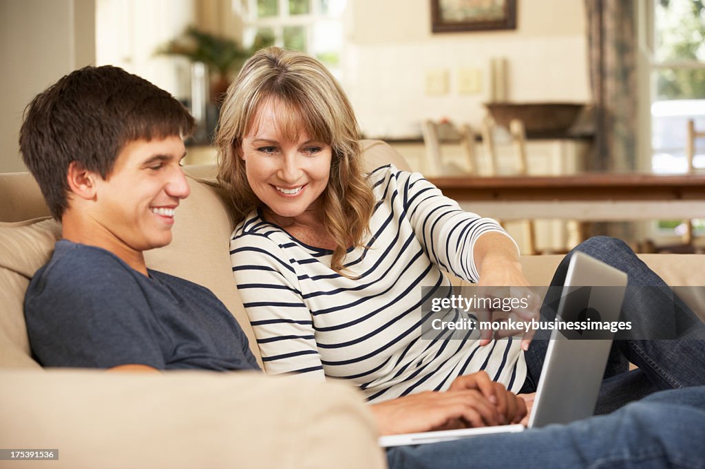 Smiling mother using laptop with teenage son on the couch