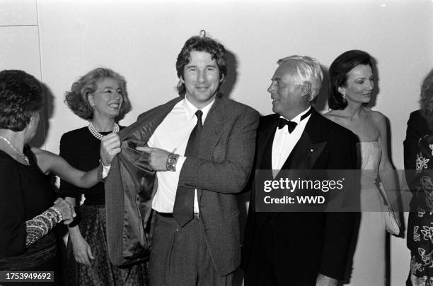 Actor Richard Gere shows designer Giorgio Armani his suit label, as guests watch the exchange, with socialite Lee Radziwill.