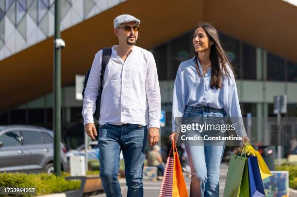 Boyfriend And Girlfriend Walking In Front Of The Shopping Mall While A Young Woman Carrying Shopping Bags High-Res Stock Photo