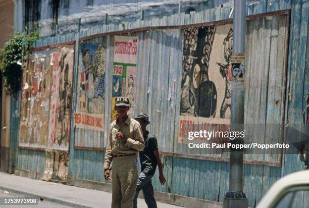 Pedestrians pass propaganda posters displayed on a street within the rebel held Caamano Zone in the city of Santo Domingo, capital of the Dominican...