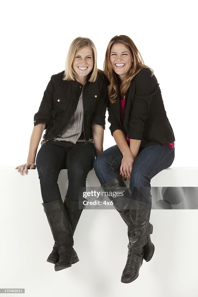 Two female friends sitting on a ledge