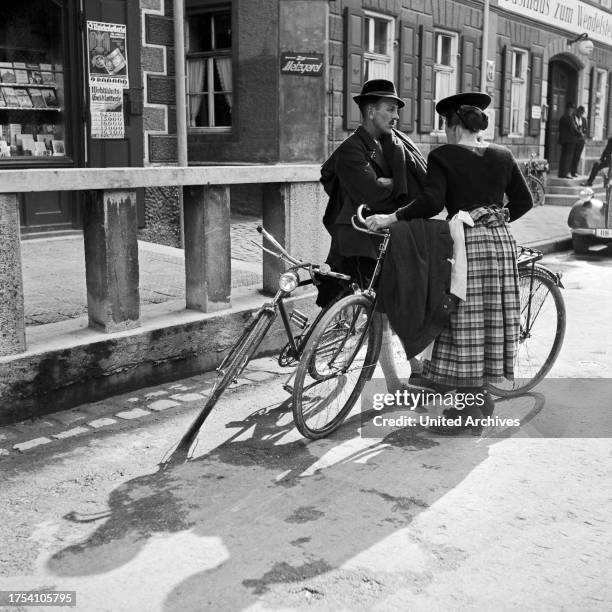 Man and a woman with their bicycles chatting on a street of Miesbach, Germany 1930s.