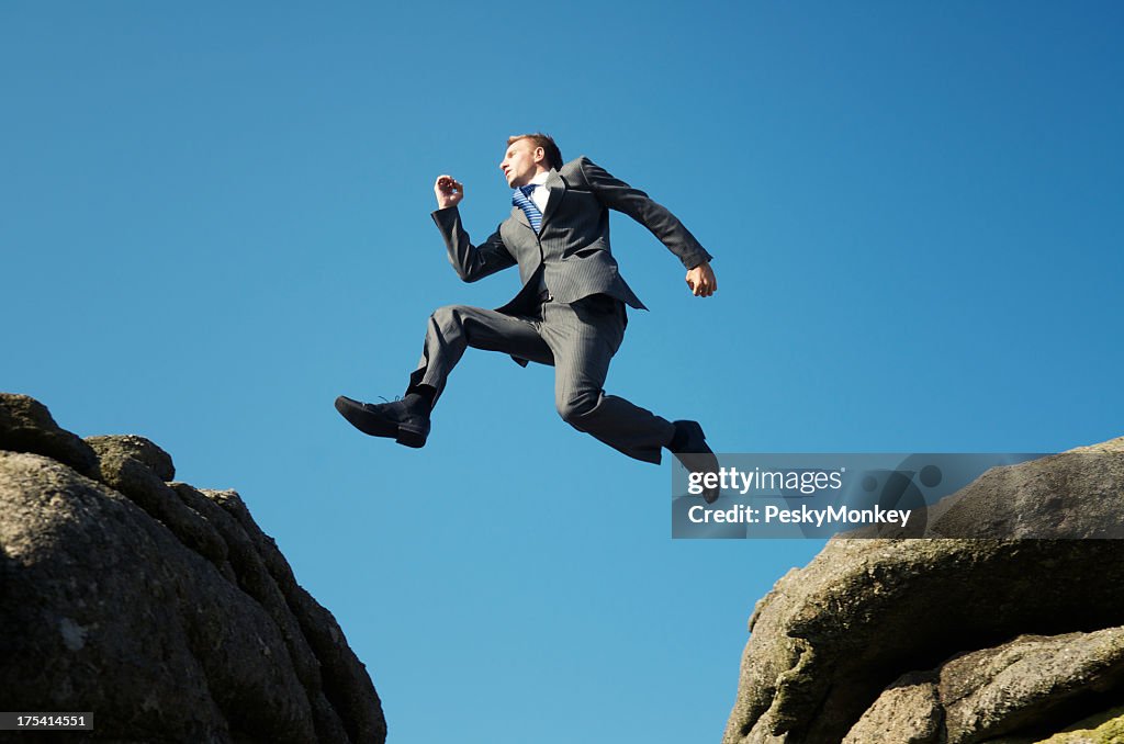 Man in suit jumping between towering rocks