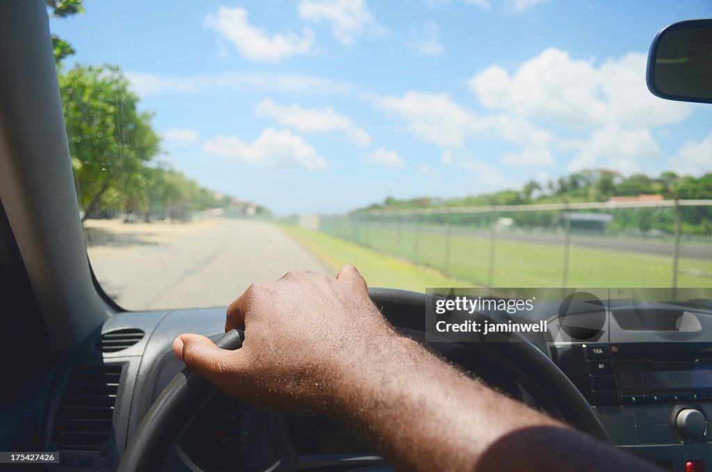 Man's hand on the steering wheel driving down a road