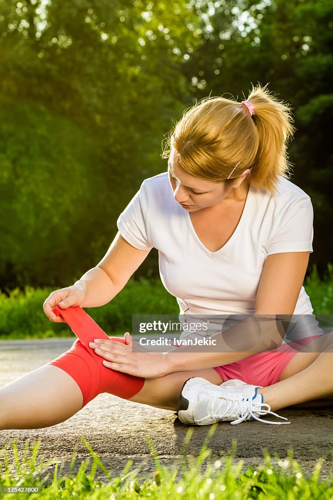 Woman bandaging her knee in red tape