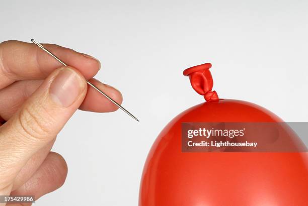 hand holding a needle about to pop a red balloon - blowing up balloon stock pictures, royalty-free photos & images