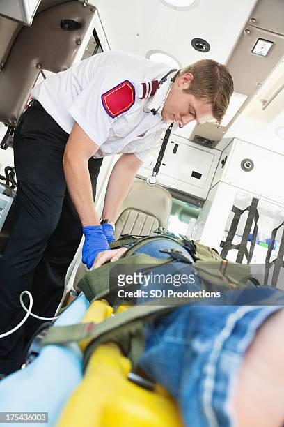medic caring for and strapping patient into ambulance stretcher - restraining device stockfoto's en -beelden