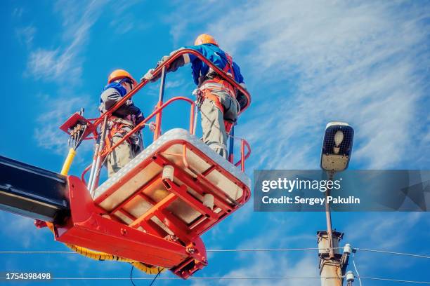 Two electricians from cradle of aerial platform or crane are repairing street lighting lamp.