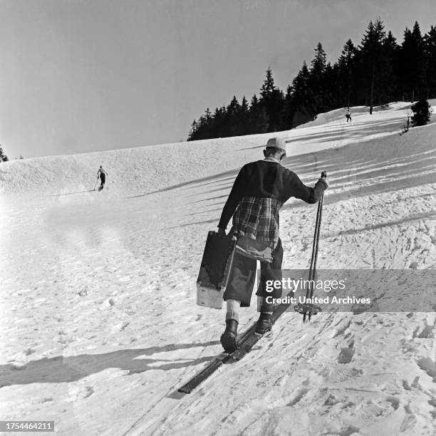 Tourist skiing with his suitcase to the hotel, Germany 1930s.
