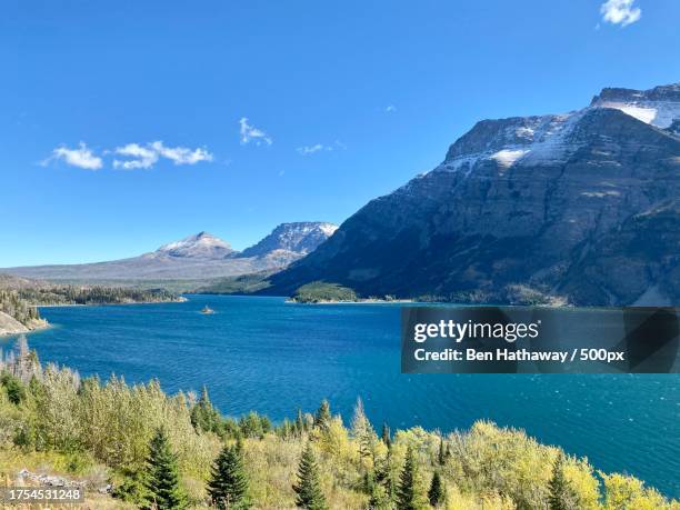 scenic view of sea and mountains against blue sky,glacier county,montana,united states,usa - glacier county montana stockfoto's en -beelden
