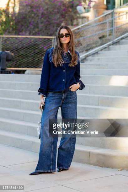 Rebeca Santana wears flared dark blue denim jeans, denim button shirt, black pointed heels, silver bag at day 1 of 080 Barcelona Fashion 2023 at...