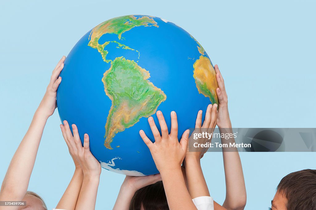 Five children's hands indoors touching a globe