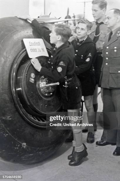 Hitler youth comparing his own height with a wheel of a Junkers JU 90 at the Wehrmacht exhibition, Germany 1940s.