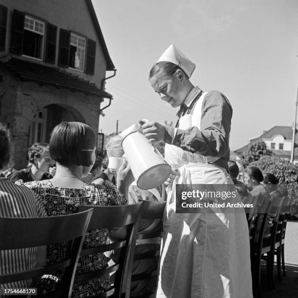 Nurse pouring coffee for women having breakfast at a mother and child recreation home at Tabarz, Thuringia.