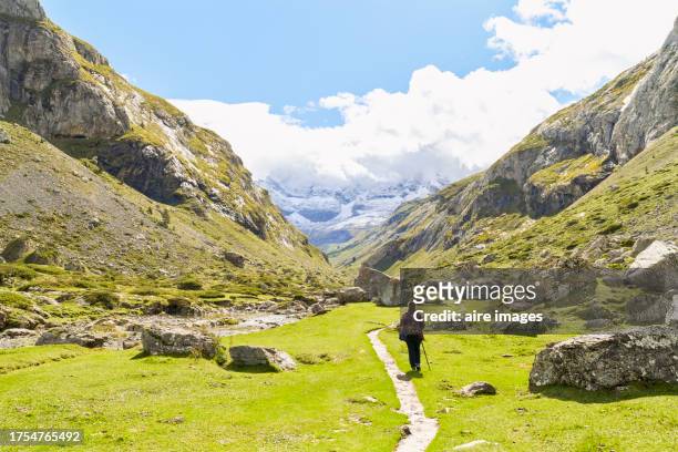 woman tourist standing with coat and walking stick smiling looking towards the camera while hiking on a mountain, pyrenees france, front view - pyrenees stock pictures, royalty-free photos & images