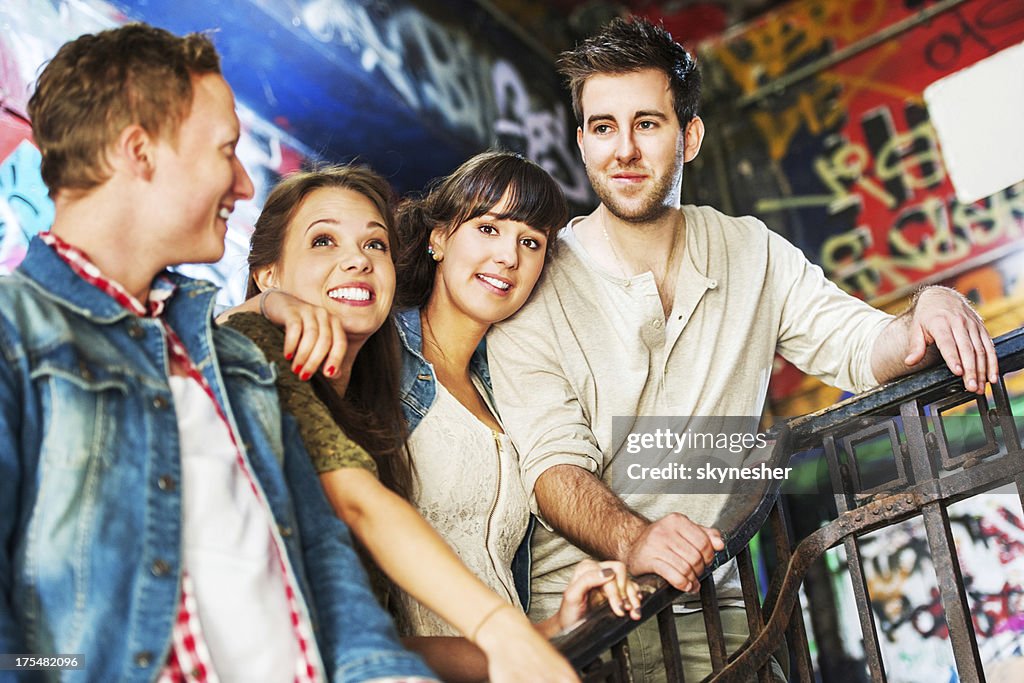 Four young people standing gegen graffiti-Wand.