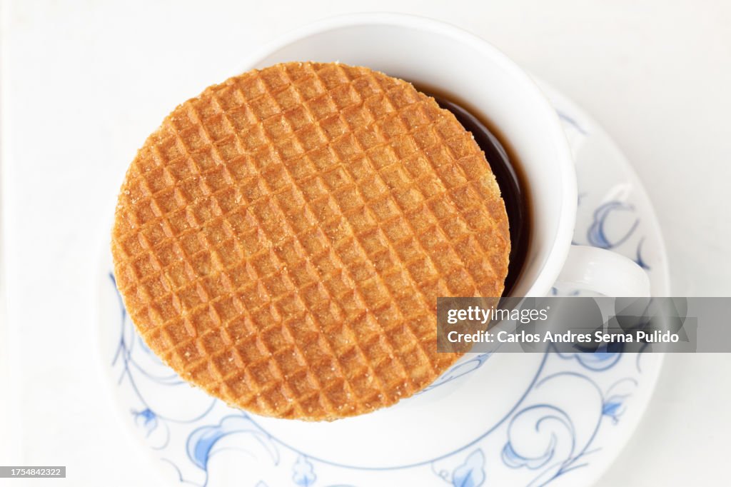 Overhead view of a Stroopwafel on a cup of coffee on a white background. Coffee time, tea time. Elegant tableware.
