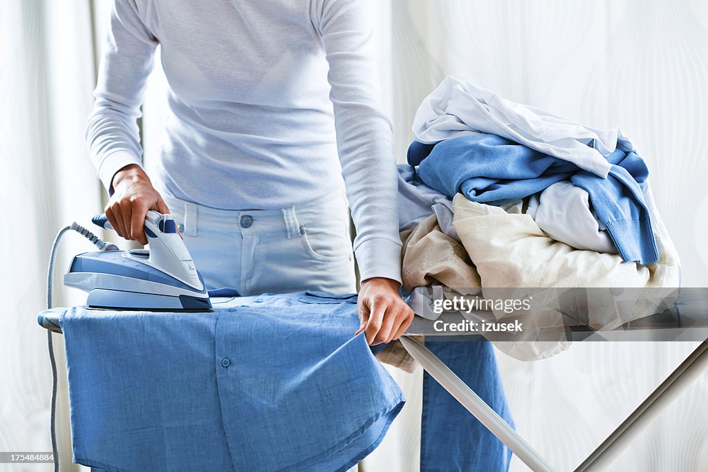 Woman Ironing Shirt Next To Pile Of Laundry