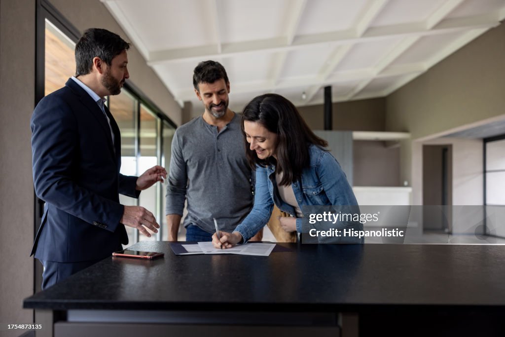 Couple buying a house and signing the deed in front of their real estate agent
