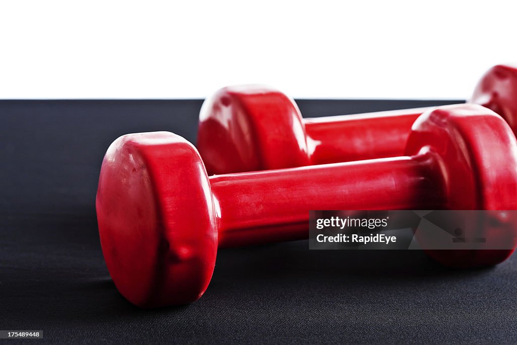 Two shiny red barbells on black surface against white