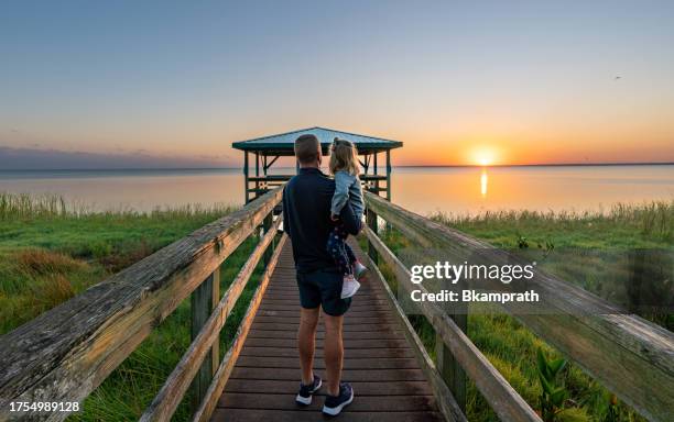vater und tochter genießen einen lebendigen sonnenaufgang über einer promenade und einem dock am lake apopka in der nähe von orlando in zentralflorida - orlando florida stock-fotos und bilder