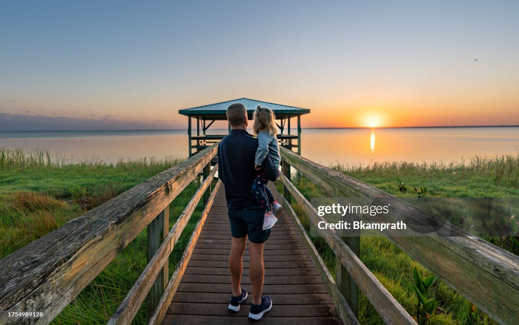 Father and Daughter Enjoying a Vibrant Sunrise Over a Boardwalk and Dock at Lake Apopka near Orlando in Central Florida