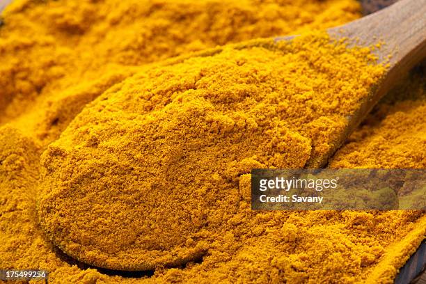 a pile of turmeric in a bowl with a wooden spoon - tumeric stock pictures, royalty-free photos & images
