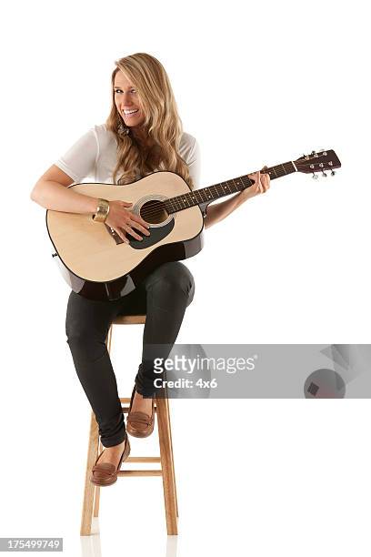attractive woman sitting on stool and playing a guitar - musician stock pictures, royalty-free photos & images