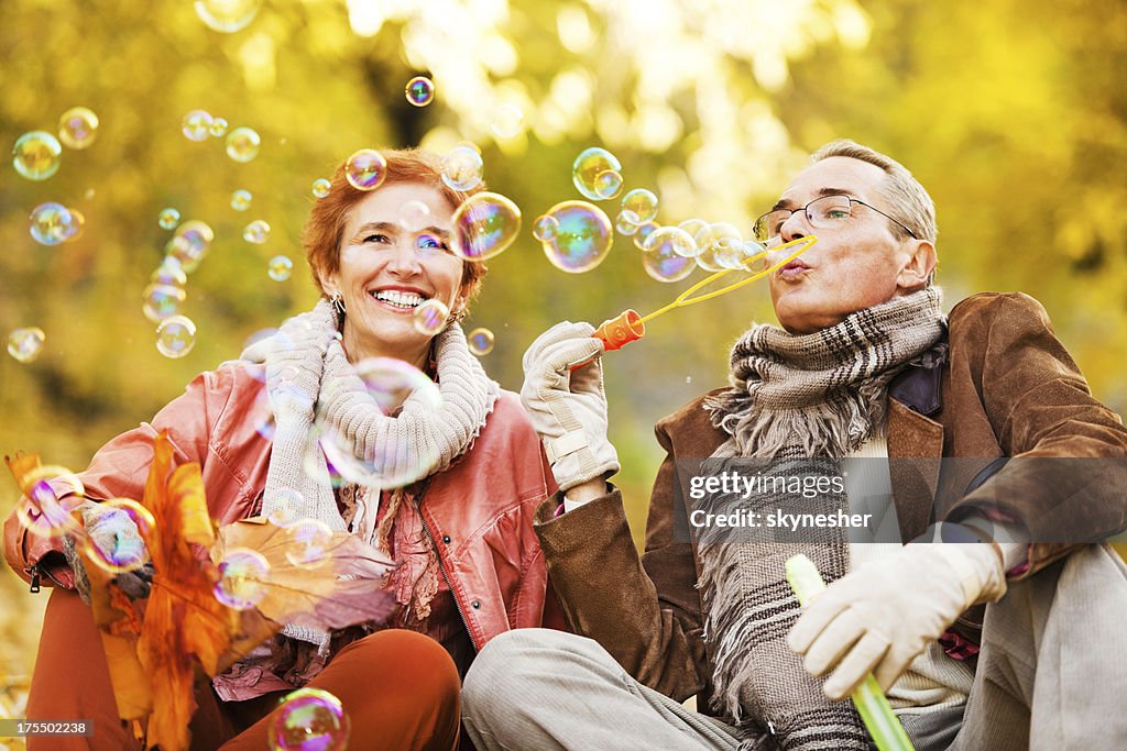 Cheerful senior couple blowing bubbles in park